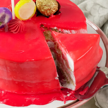A slice of red drip cake being removed from the main cake on a cake stand