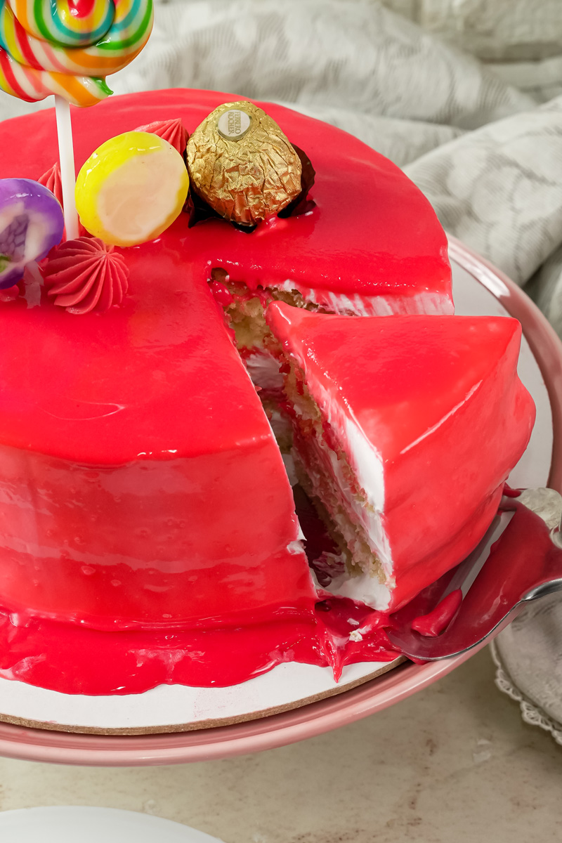 A slice of red drip cake being removed from the main cake on a cake stand