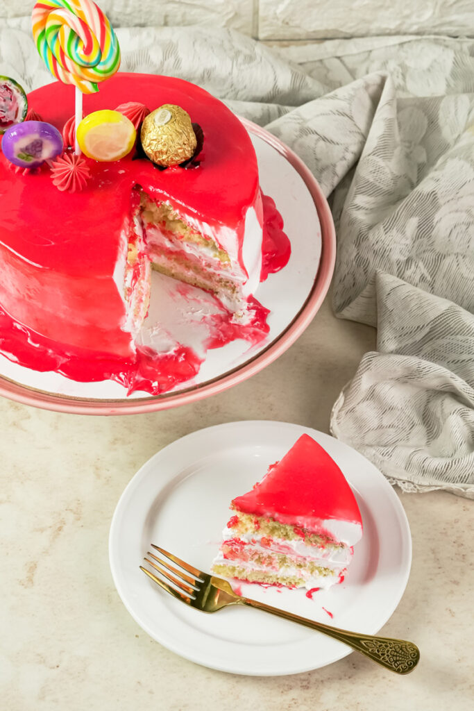 A slice of red drip cake on a plate next to the main cake