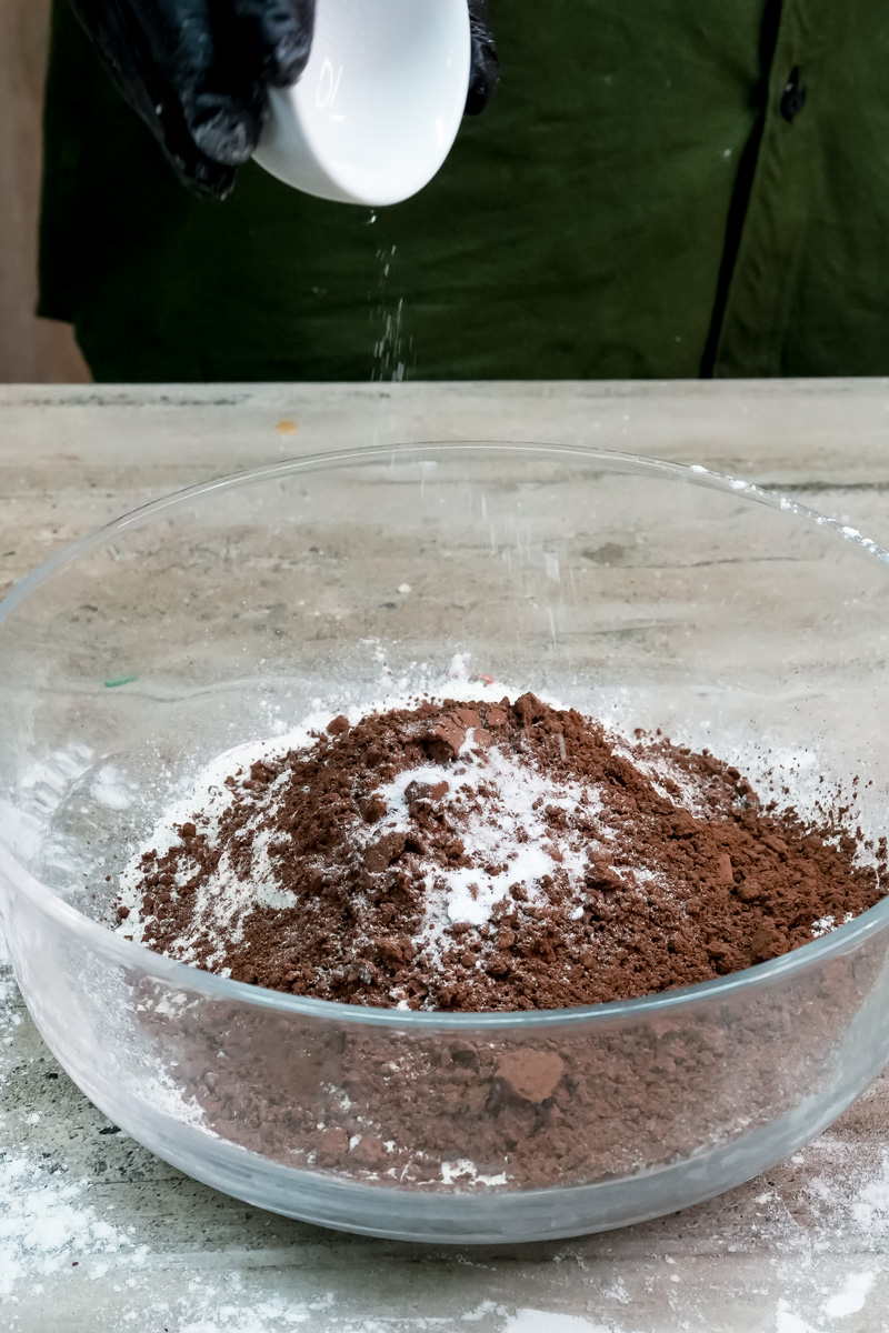 Adding baking powder to a bowl of flour and cocoa powder