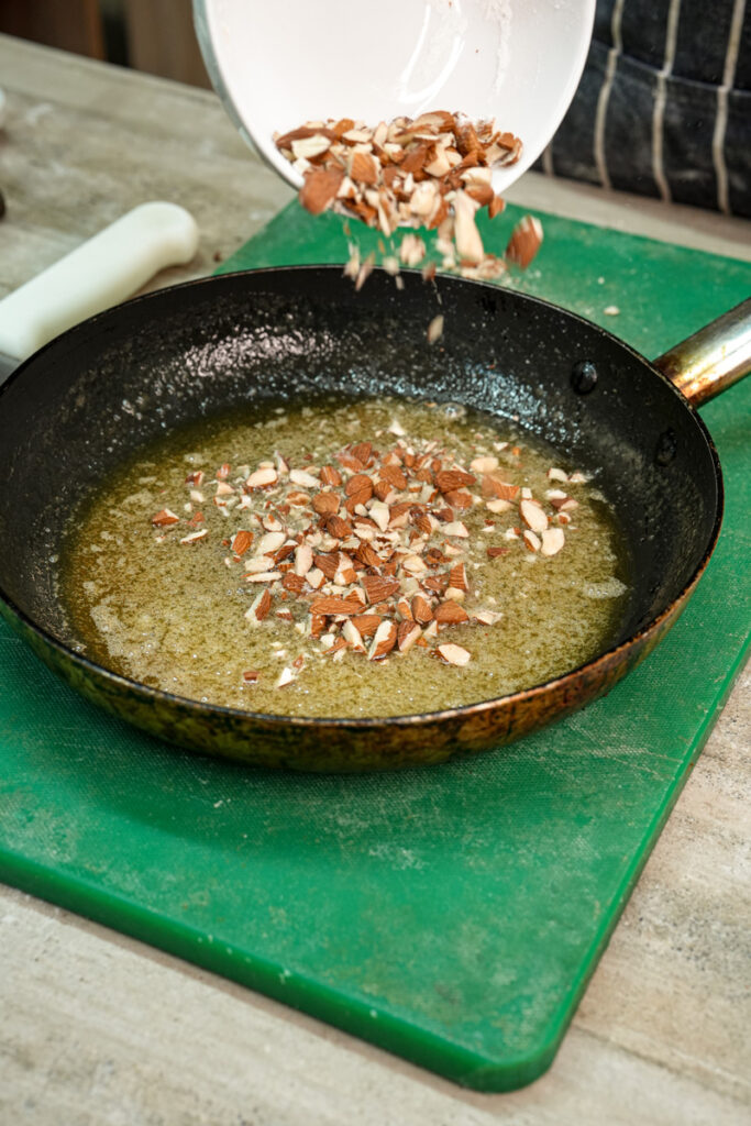 Adding chopped almonds to melted butter in skillet for bee sting cake topping