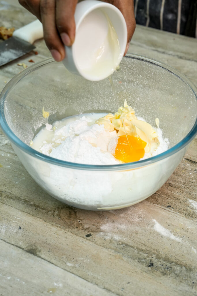 Adding egg to pineapple bun dough ingredients in mixing bowl