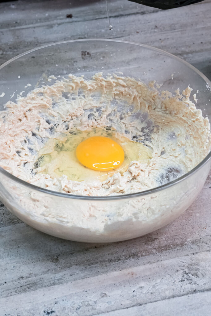 Adding egg to ranger cookie dough mixture in mixing bowl