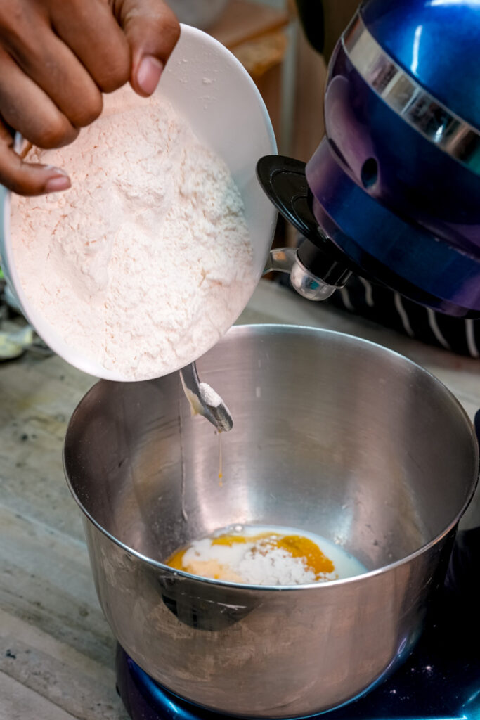 Adding flour to pineapple bun dough ingredients in mixer bowl