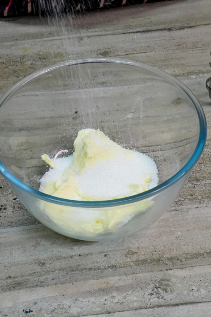 Adding granulated sugar to creamed butter in a glass bowl