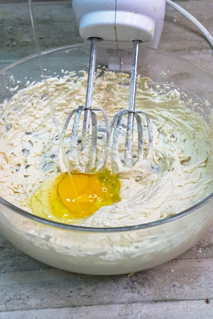 An egg being cracked into the creamed butter and sugar mixture