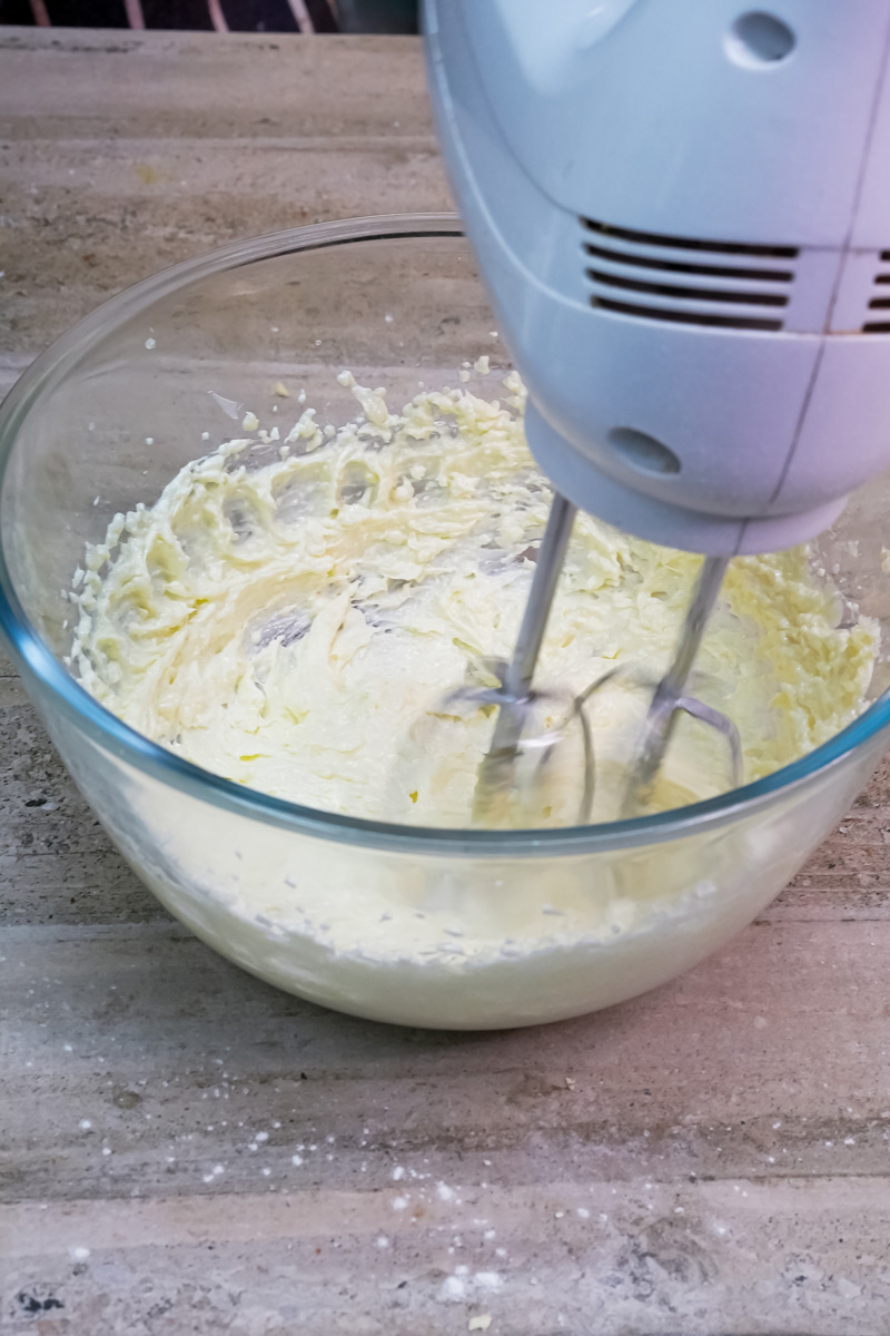 An electric hand mixer creaming together butter and sugar in a glass bowl to create the base for the oatmeal cookie dough