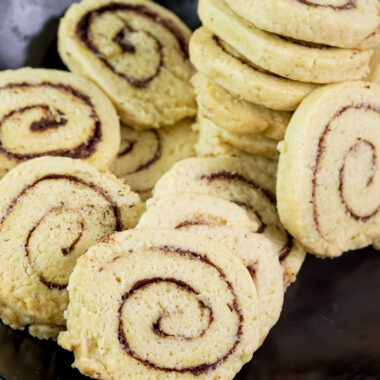 A stack of baked cinnamon roll cookies in a black bowl, showcasing the swirl