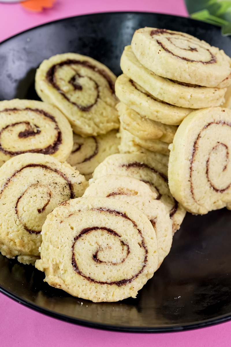 A stack of baked cinnamon roll cookies in a black bowl, showcasing the swirl