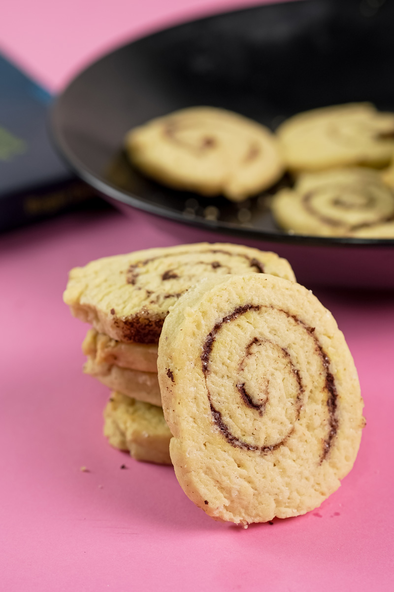 Baked cinnamon roll cookies in a stack with a blurry plate in the background