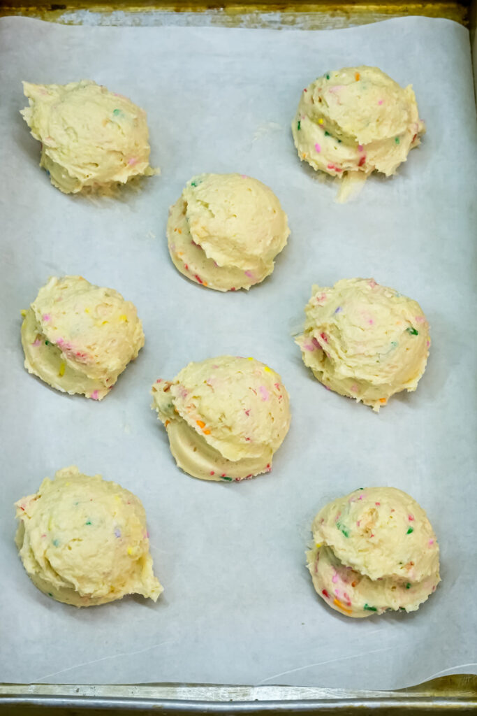 Balls of Funfetti cookie dough ready for baking on a parchment-lined sheet