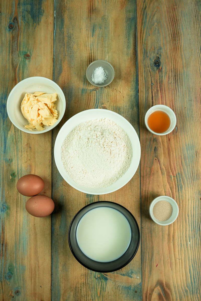 Bee sting cake ingredients laid out on wooden surface - flour, eggs, milk, butter, honey, salt and yeast