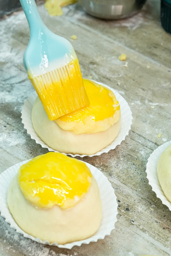 Brushing egg wash on pineapple buns before baking