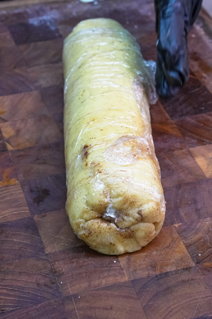 Chilled cookie dough log wrapped in plastic, ready to be sliced