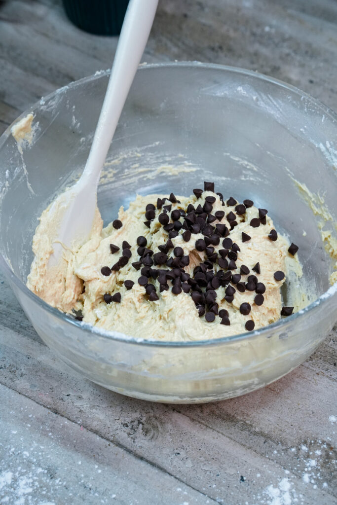 Chocolate chips being folded into the cookie dough with a spatula