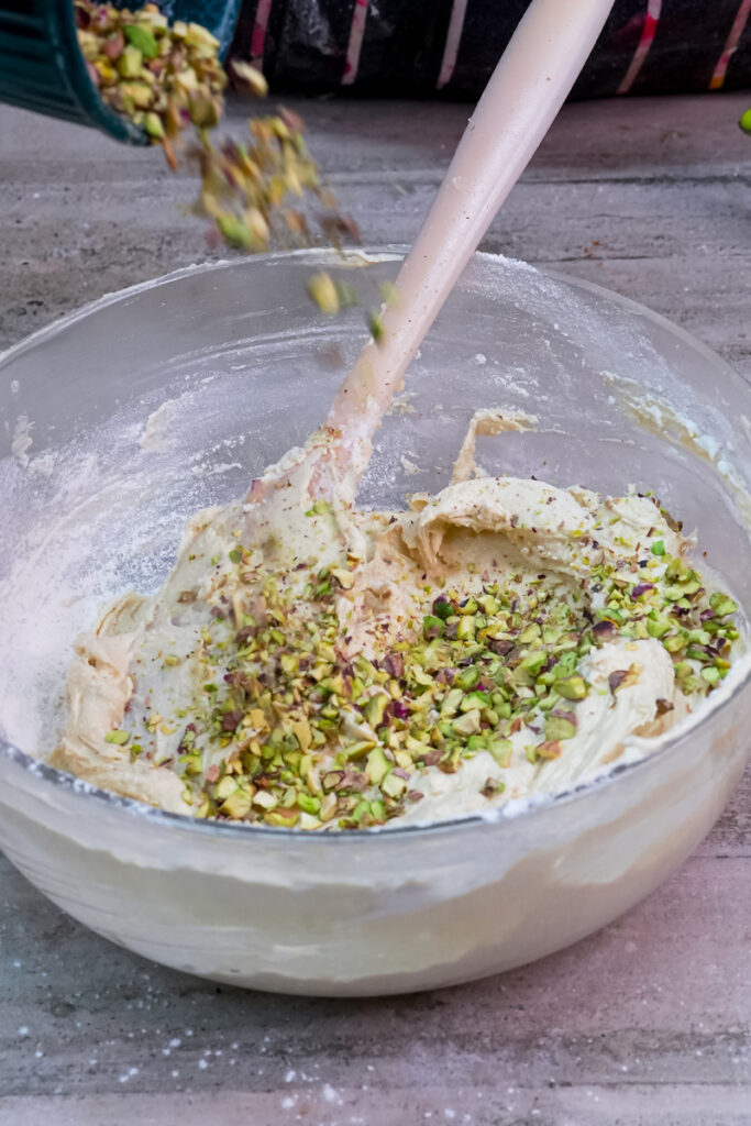 Chopped pistachios being poured into the cookie dough