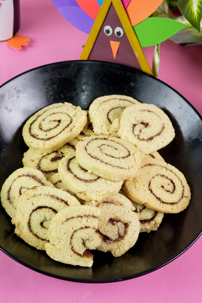 Cinnamon roll cookies in a black bowl against a pink background