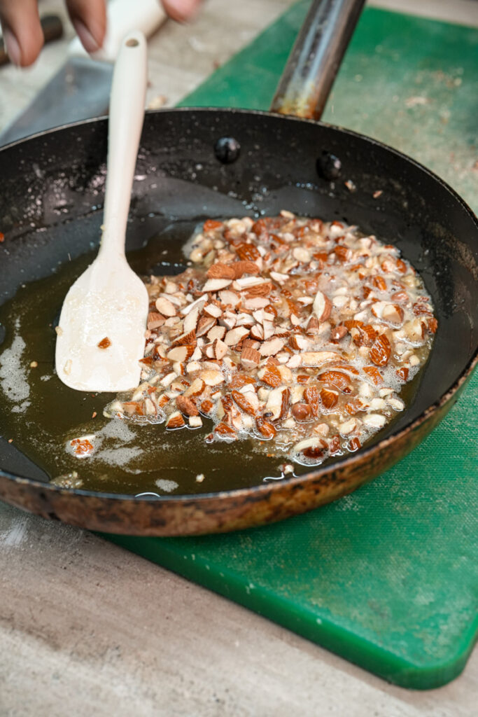 Cooking honey almond topping in skillet with wooden spoon for bee sting cake