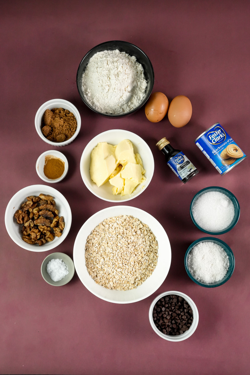 Cowboy cookie ingredients laid out - flour, oats, chocolate chips, butter, eggs, spices