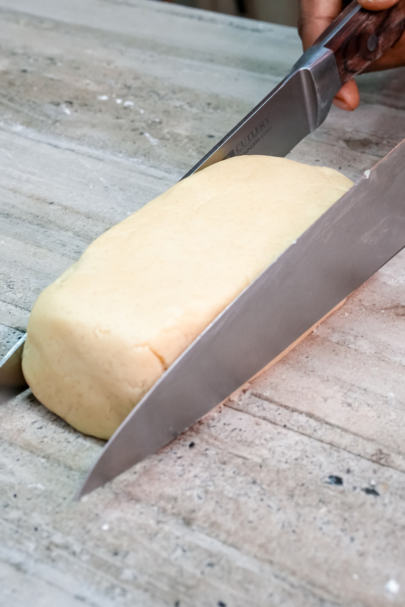 Cutting shortbread cookie log with sharp knife on cutting board