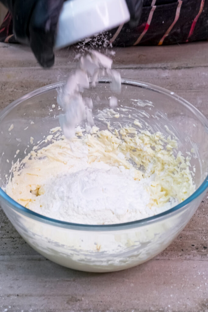 Dry ingredients, including flour and baking powder, being poured into the wet mixture in a glass bowl