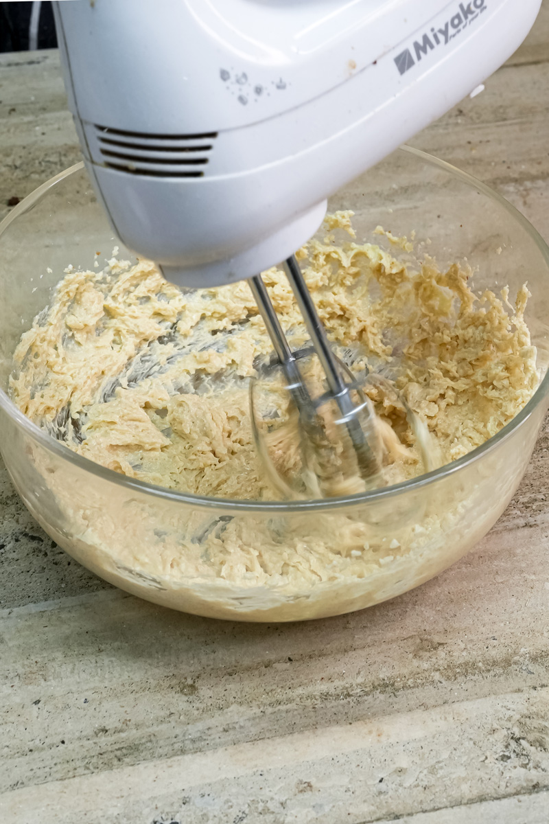 Electric hand mixer beating cookie dough in clear glass bowl