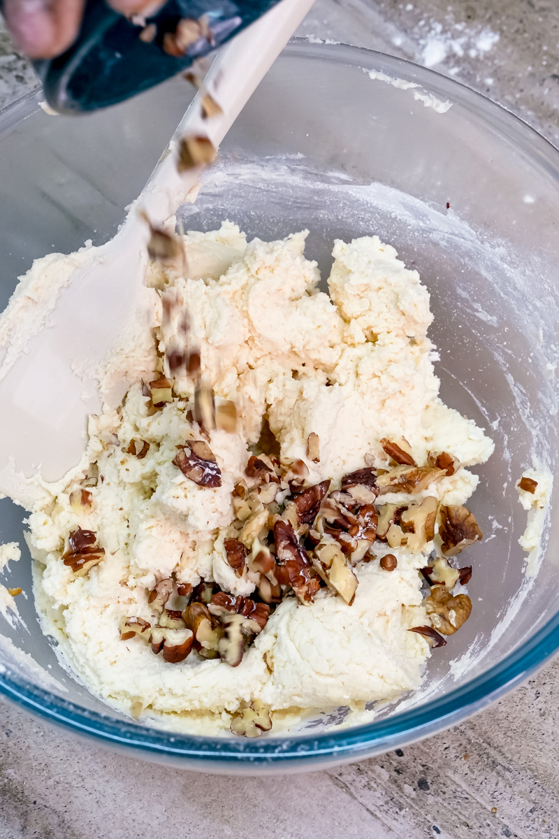 Folding chopped walnuts into Mexican wedding cookie dough with wooden spoon