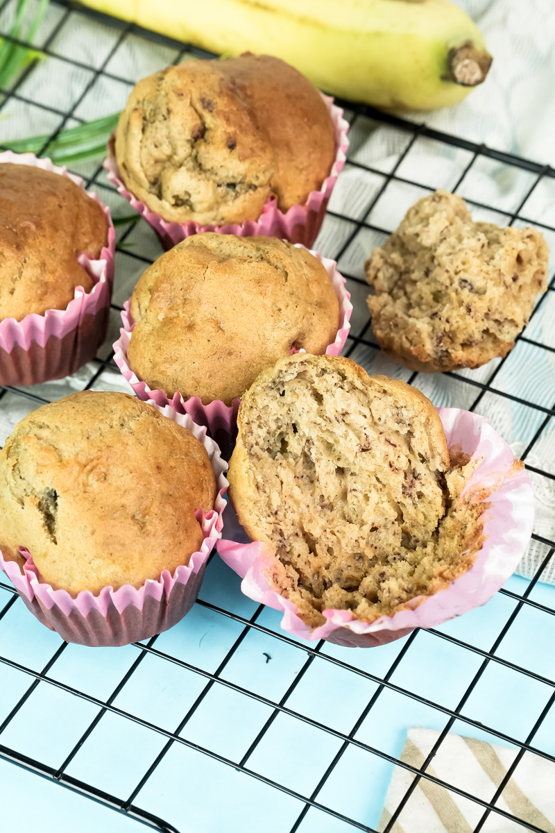 Four whole banana muffins and one split in half on a cooling rack