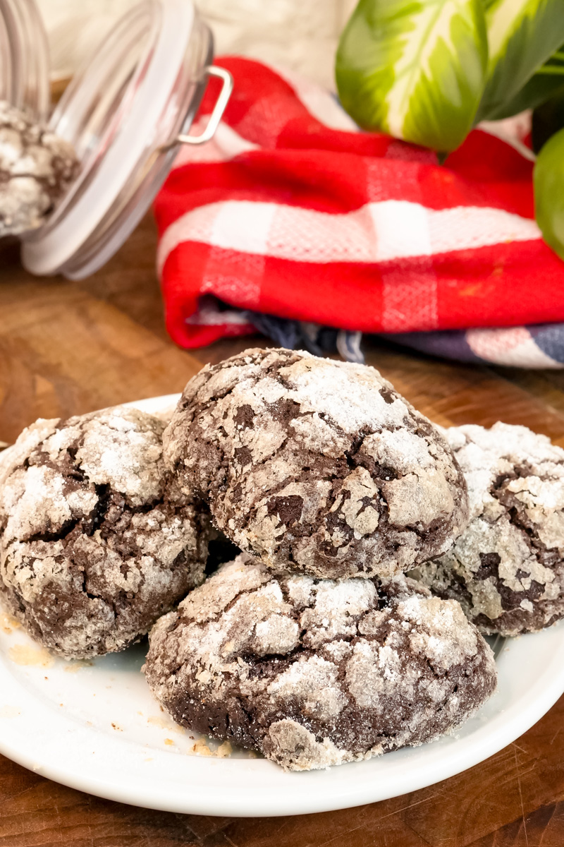 Six chocolate crinkle cookies, rolled in powdered sugar, ready to be baked on a parchment-lined tray.