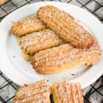 Freshly baked churro cookies on a white plate, with one broken in half to show the soft inside