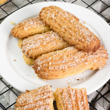 Freshly baked churro cookies on a white plate, with one broken in half to show the soft inside