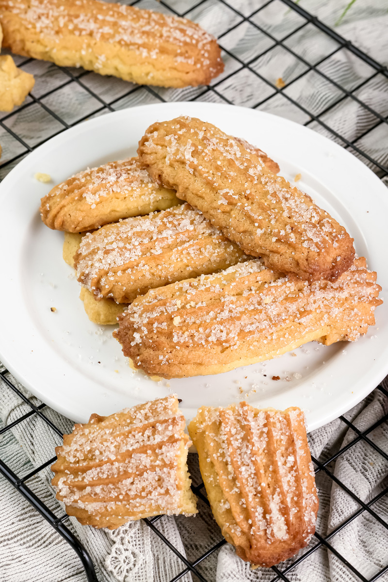 Freshly baked churro cookies on a white plate, with one broken in half to show the soft inside