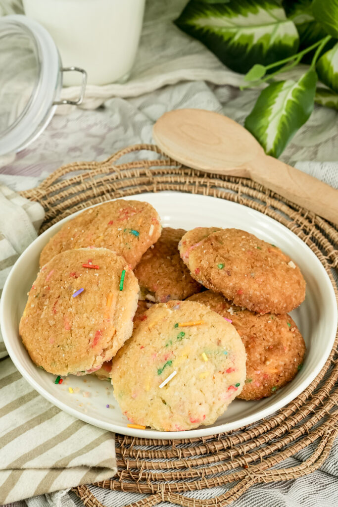 Funfetti cookies arranged on a plate with a jar and a wooden spoon in the background