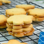 Golden alfajores sandwich cookies filled with caramel on cooling rack