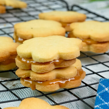 Golden alfajores sandwich cookies filled with caramel on cooling rack
