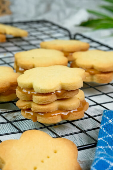 Golden alfajores sandwich cookies filled with caramel on cooling rack