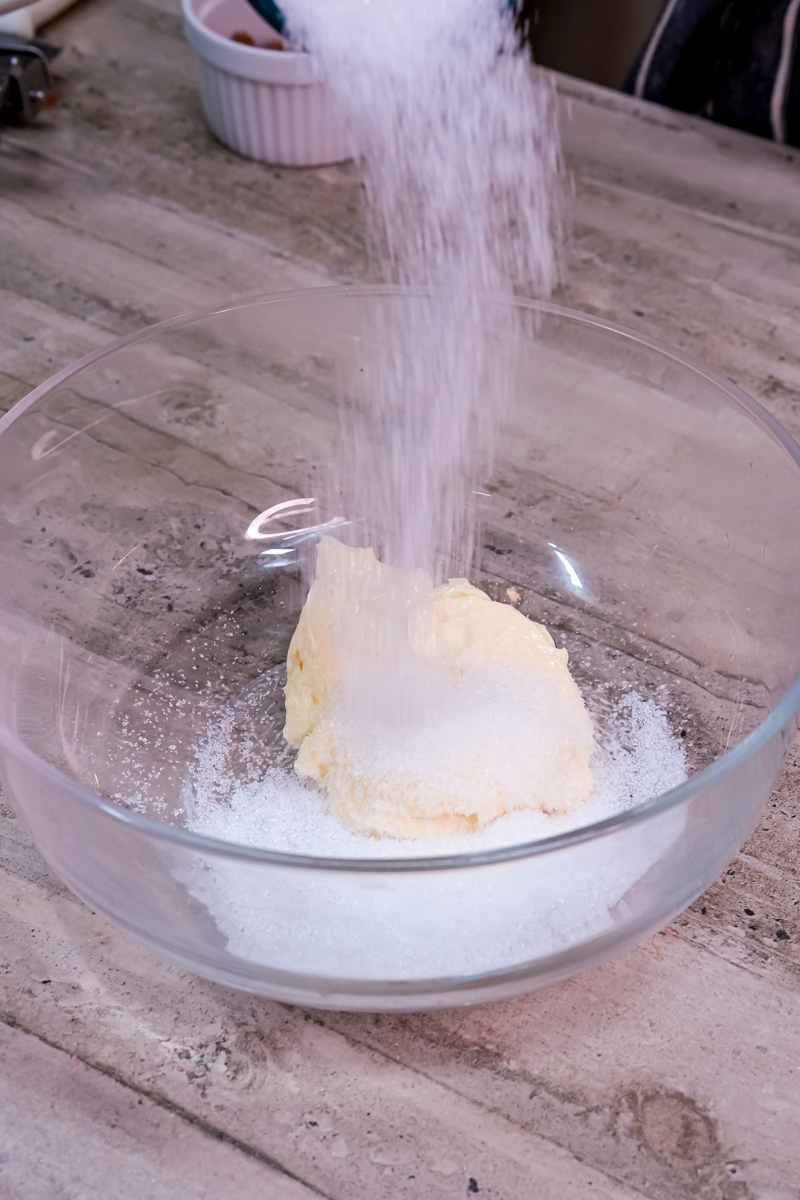 Granulated sugar being poured into a bowl with butter