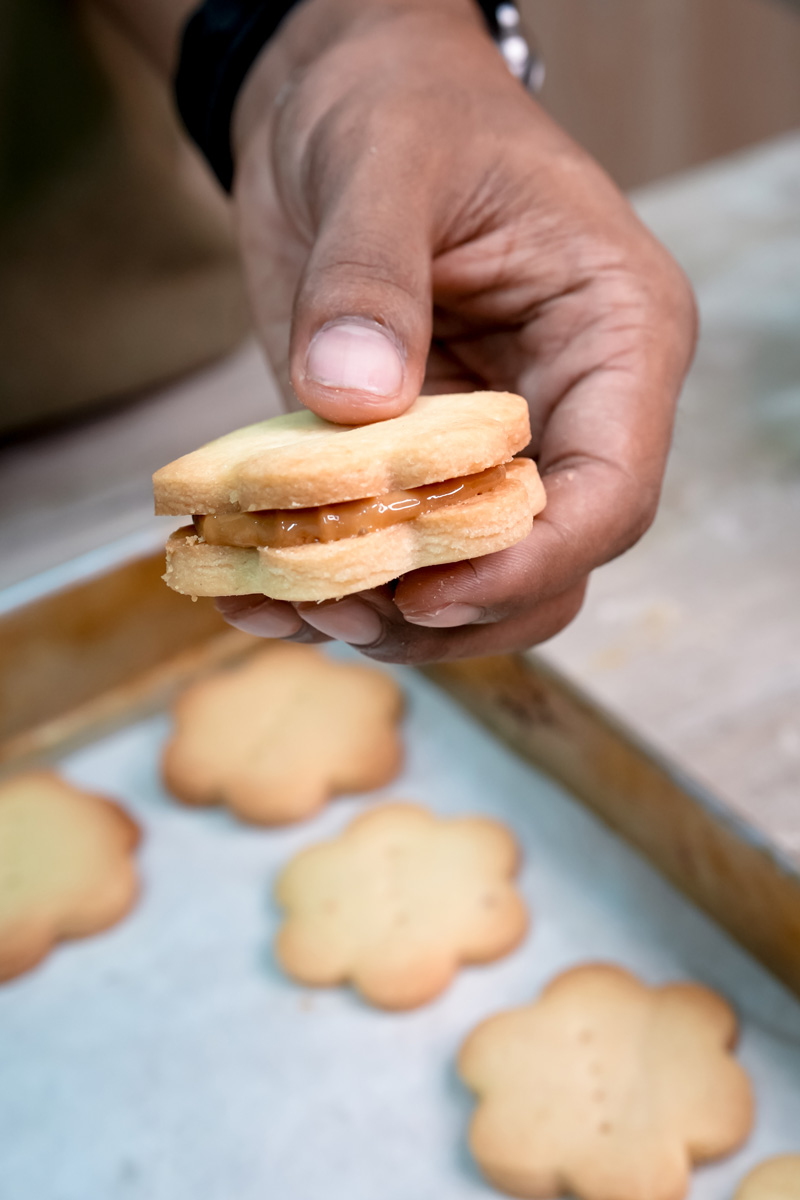 Hand holding freshly made alfajor cookie showing dulce de leche filling