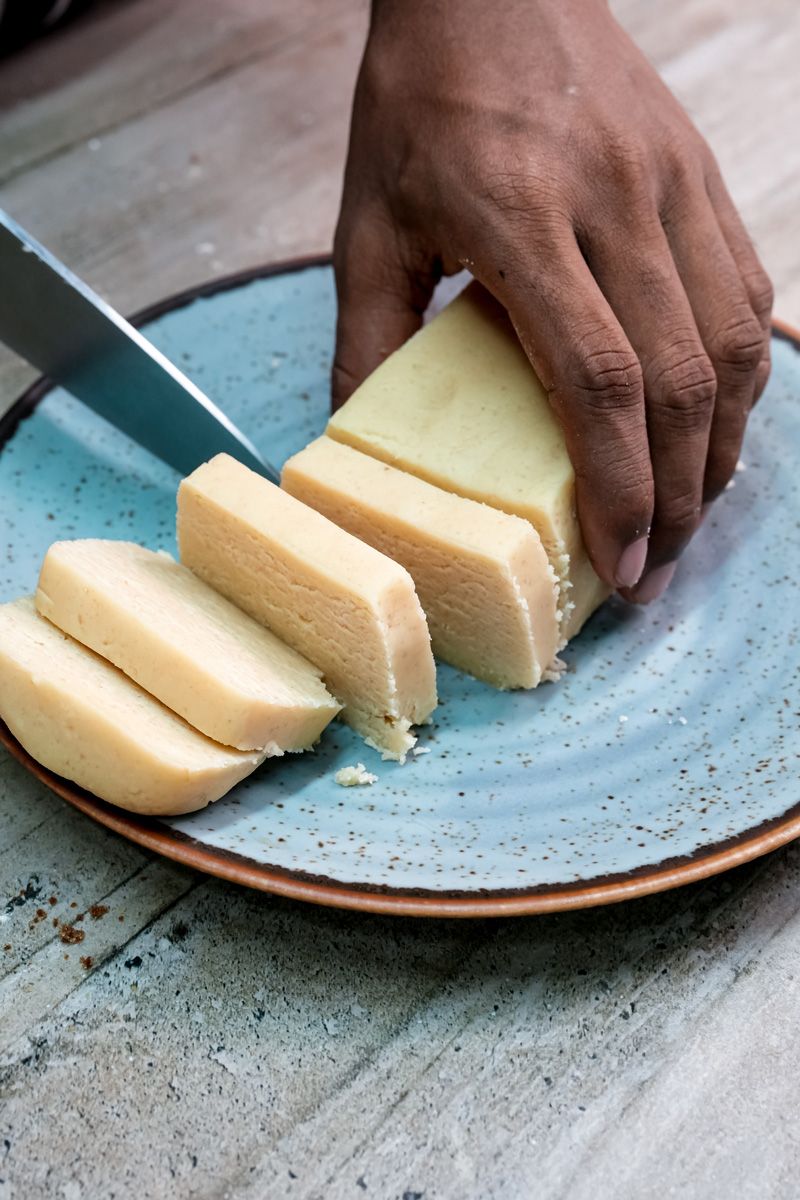 Hand slicing homemade shortbread cookie dough on blue speckled plate