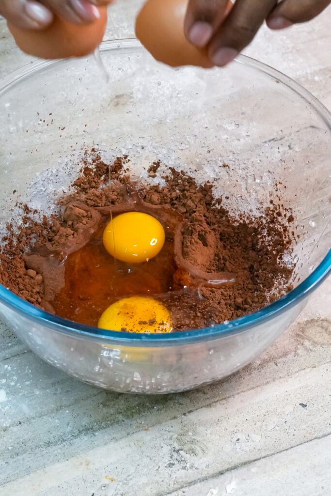 Hands cracking a second egg into the chocolate crinkle cookie dough mixture