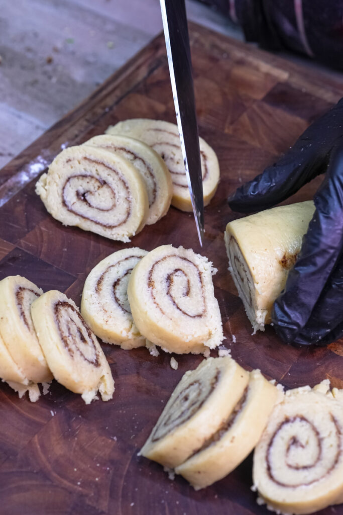 Hands slicing the chilled dough log into cinnamon roll cookies on a wooden board