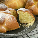 Homemade Pan de Muerto breads cooling on wire rack with torn piece showing crumb structure