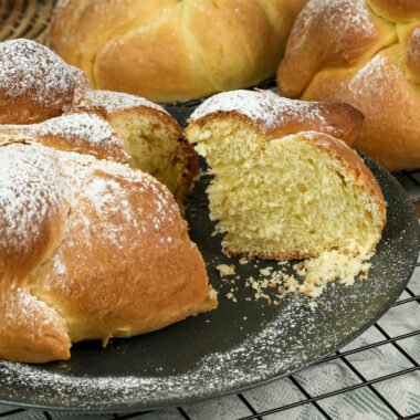Homemade Pan de Muerto breads cooling on wire rack with torn piece showing crumb structure