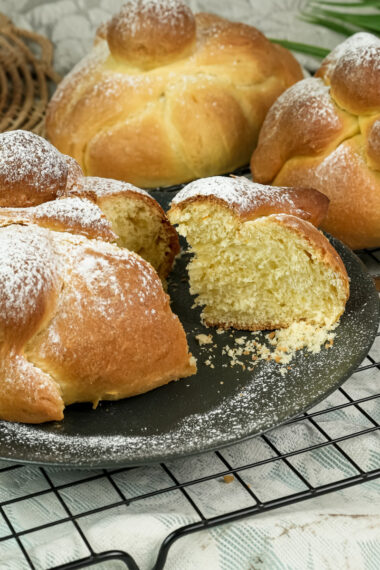 Homemade Pan de Muerto breads cooling on wire rack with torn piece showing crumb structure