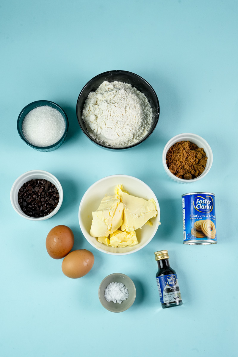 Ingredients for chocolate chip cookies laid out on a blue surface