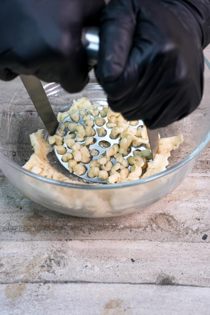 Mashing ripe bananas with a potato masher in a glass bowl for a muffin recipe