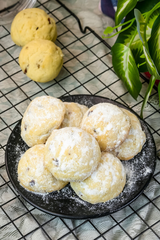 Mexican wedding cookies with powdered sugar coating on black plate with cooling rack
