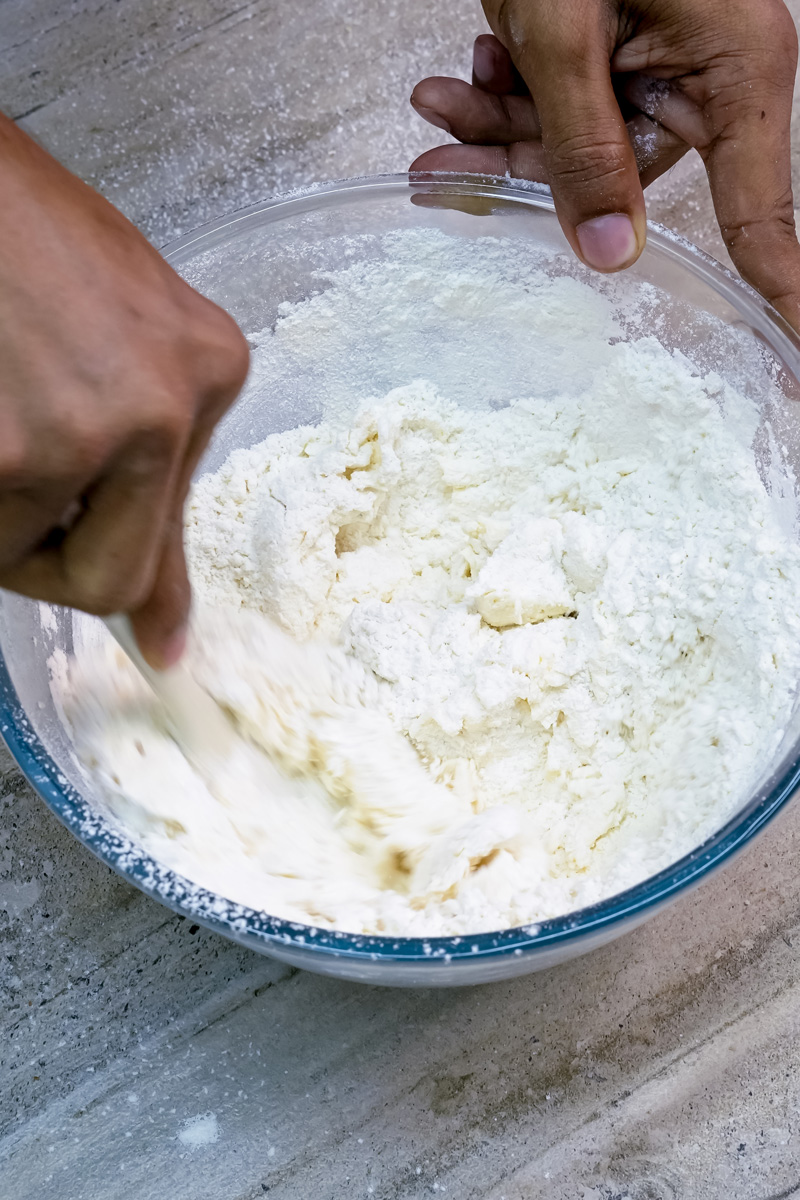 Mixing Mexican wedding cookie dough by hand in glass bowl