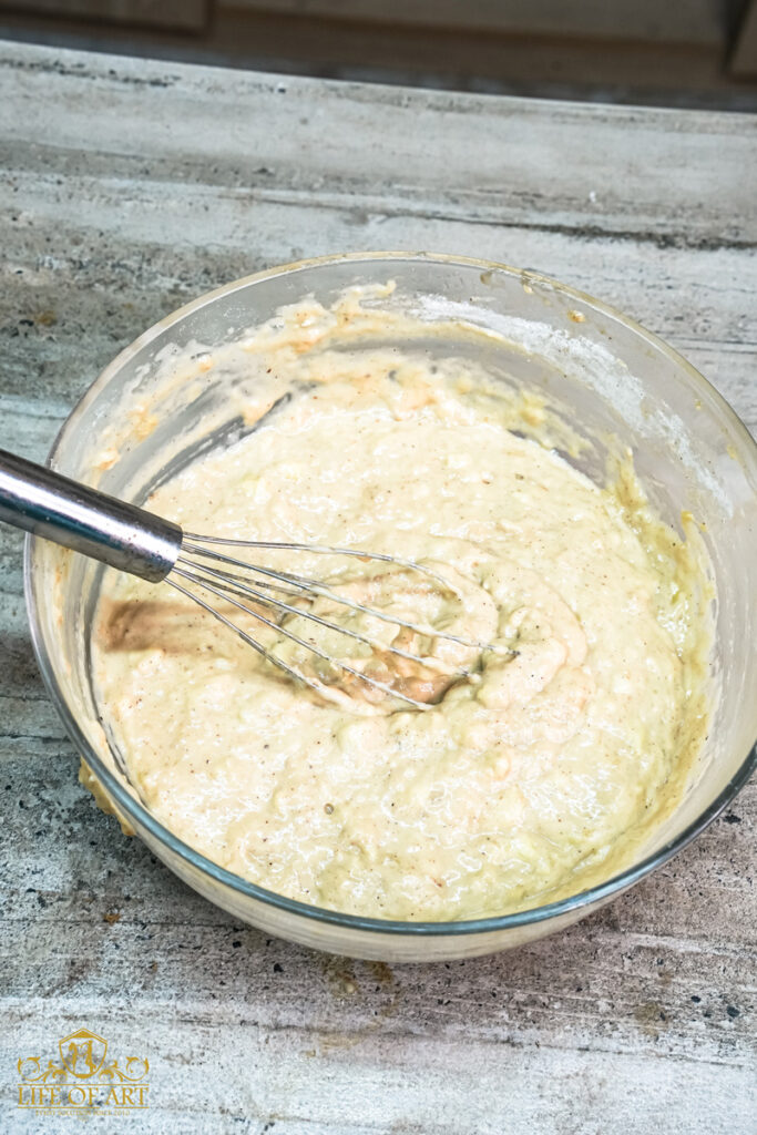 Mixing banana muffin batter in a glass bowl with a whisk