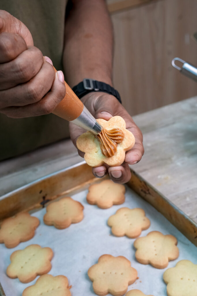 Piping dulce de leche filling onto alfajores cookie base